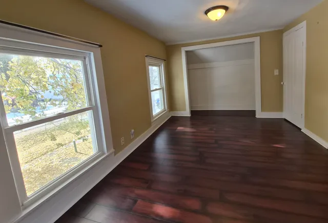 a view of an empty room with wooden floor and a window
