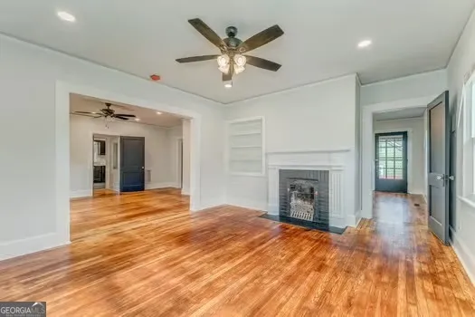 a view of an empty room with chandelier fan and wooden floor