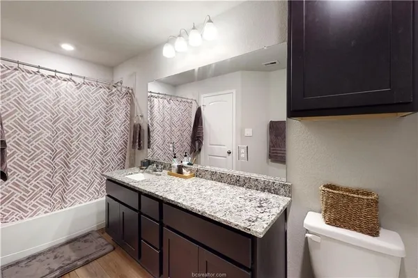 a bathroom with a granite countertop sink a toilet a mirror and shower