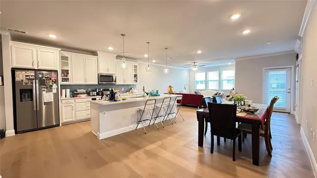 a kitchen with stainless steel appliances kitchen island granite countertop a dining table chairs refrigerator and cabinets