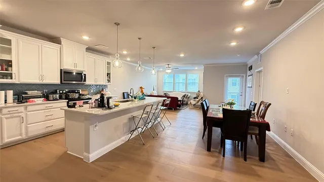 a large white kitchen with stainless steel appliances granite countertop a stove a sink a dining table and chairs with wooden floor