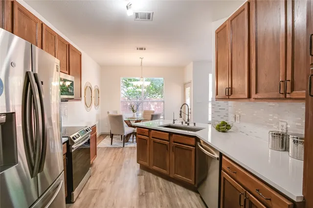 a kitchen with stainless steel appliances granite countertop a refrigerator a sink dishwasher a stove and white countertops with wooden floor