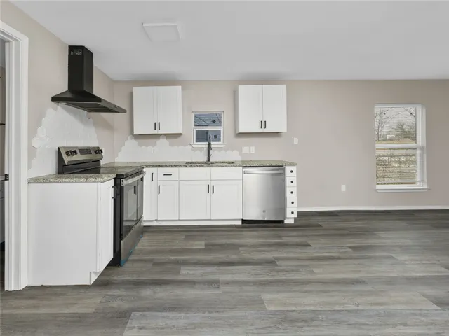 a kitchen with stainless steel appliances granite countertop a sink stove and white cabinets with wooden floor