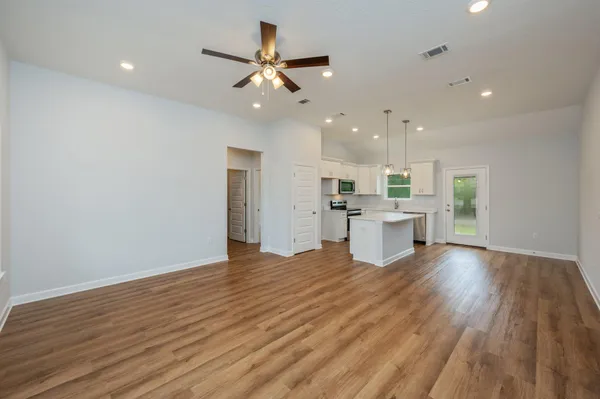 a view of an empty room with wooden floor and a kitchen