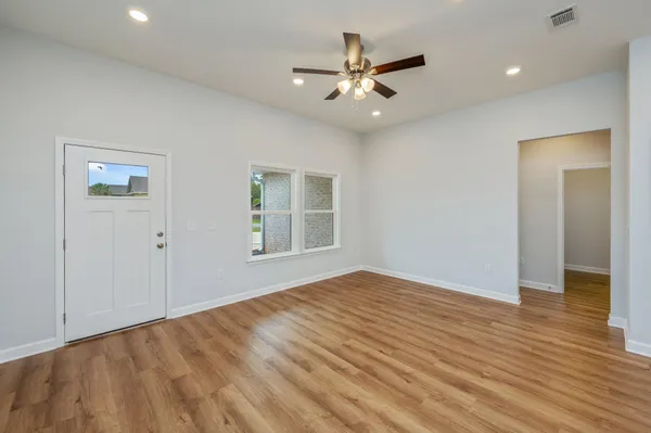 a view of an empty room with wooden floor and a ceiling fan