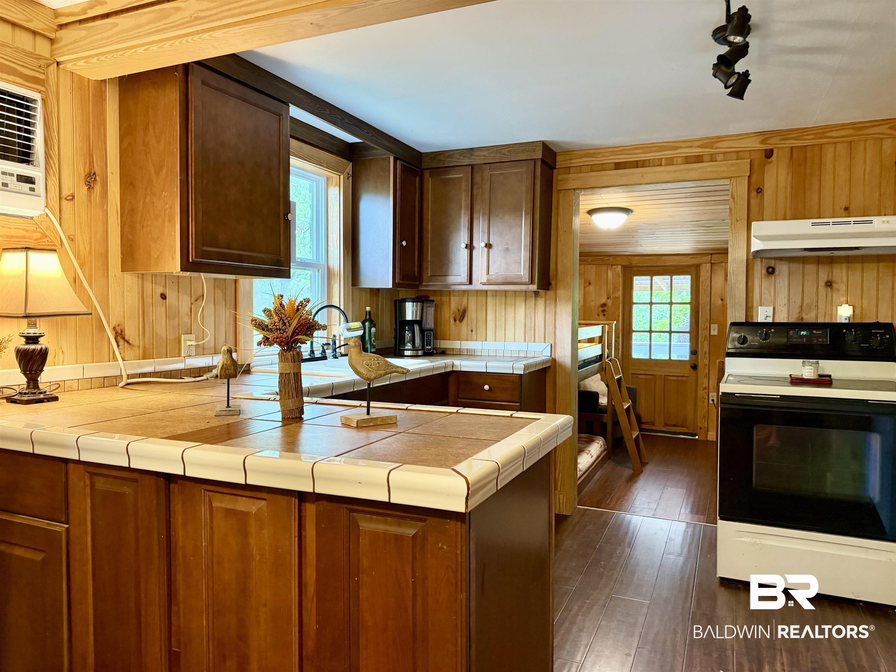 762 Buddy Lake Road Brewton, AL 36426 - Photo 7 of 20 Kitchen featuring wood paneling, tile countertops, wood-finish flooring, dark wood cabinetry, and white appliances