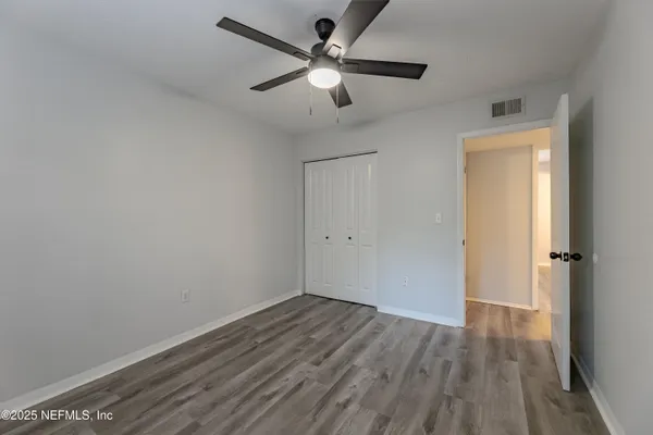 an empty room with wooden floor ceiling fan and windows