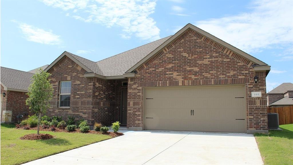 Brick veneer exterior featuring a two-car garage with a tan door, a concrete driveway, and a landscaped front yard with a young tree