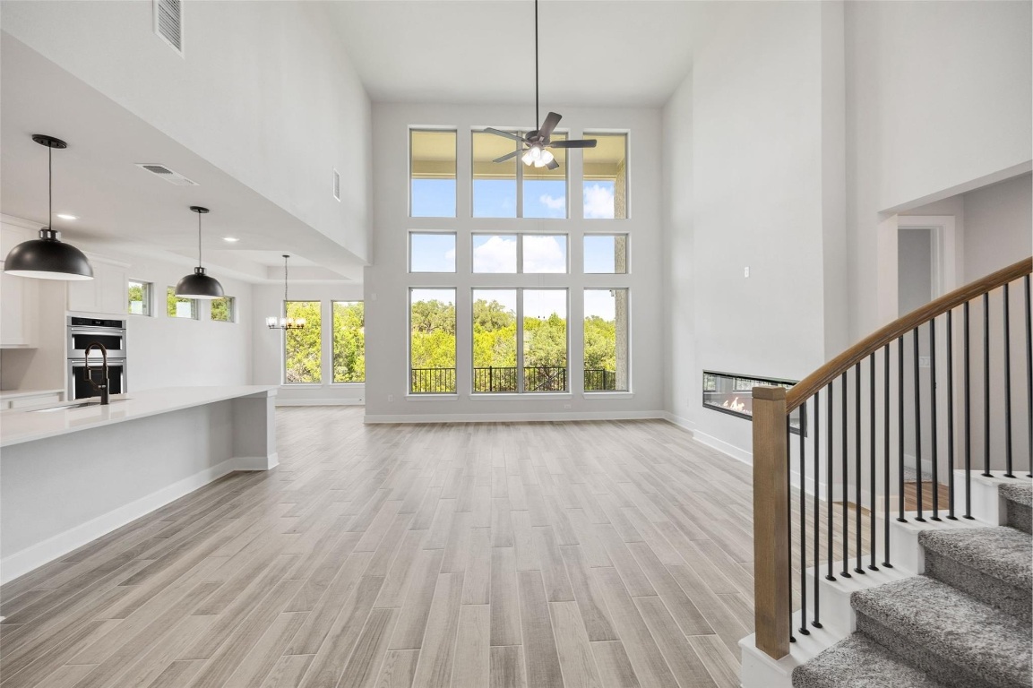 1417 Rodeo Ridge Drive Georgetown, TX 78628 - Photo 5 of 37 Unfurnished living room featuring a glass covered fireplace, a towering ceiling, light wood-style flooring, a ceiling fan, and a chandelier