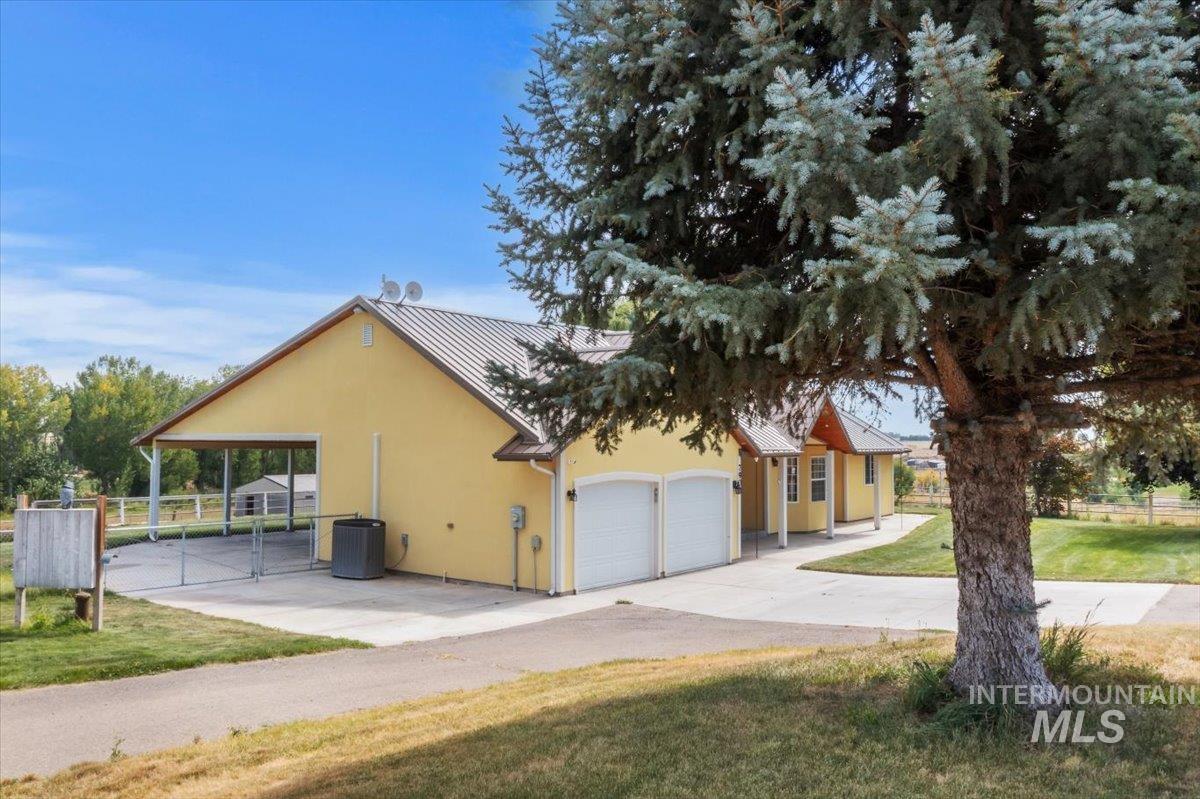 7900 Labor Camp Road Caldwell, ID 83607 - Photo 38 of 45 Two-car garage with arched entryways, covered carport, yellow stucco exterior, and metal roofing
