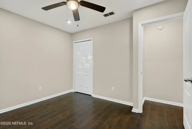 an empty room with wooden floor ceiling fan and windows