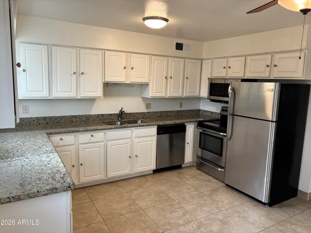 a kitchen with granite countertop a refrigerator sink and white cabinets