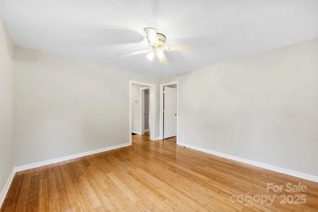 a view of an empty room with wooden floor and a ceiling fan