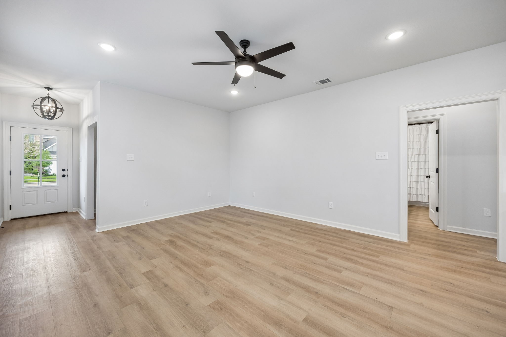 10902 Bonfire Trail Beasley, TX 77417 - Photo 3 of 36 This spacious, light-filled room features modern vinyl plank flooring, a ceiling fan, and recessed lighting. The entryway has a stylish light fixture, and there's a view of a bathroom through an open door. The neutral palette offers a versatile space ready for personal touches.