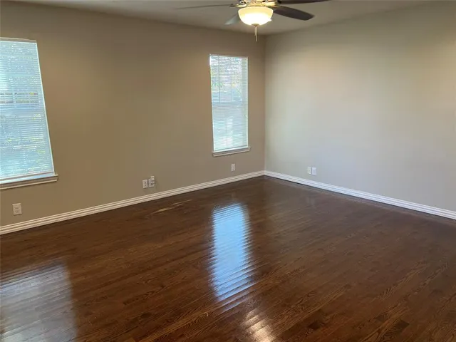 an empty room with wooden floor chandelier fan and windows