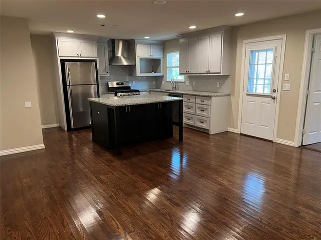 a kitchen with stainless steel appliances granite countertop a refrigerator a sink dishwasher a stove and white countertops with wooden floor