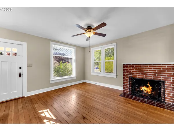 a view of an empty room with wooden floor fireplace and a window