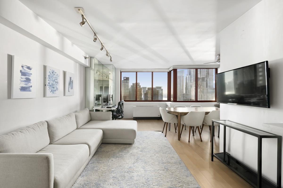 4-74 48th Avenue, Unit 26J Queens, NY 11109 - Photo 3 of 7 a living room with furniture a flat screen tv and a large window