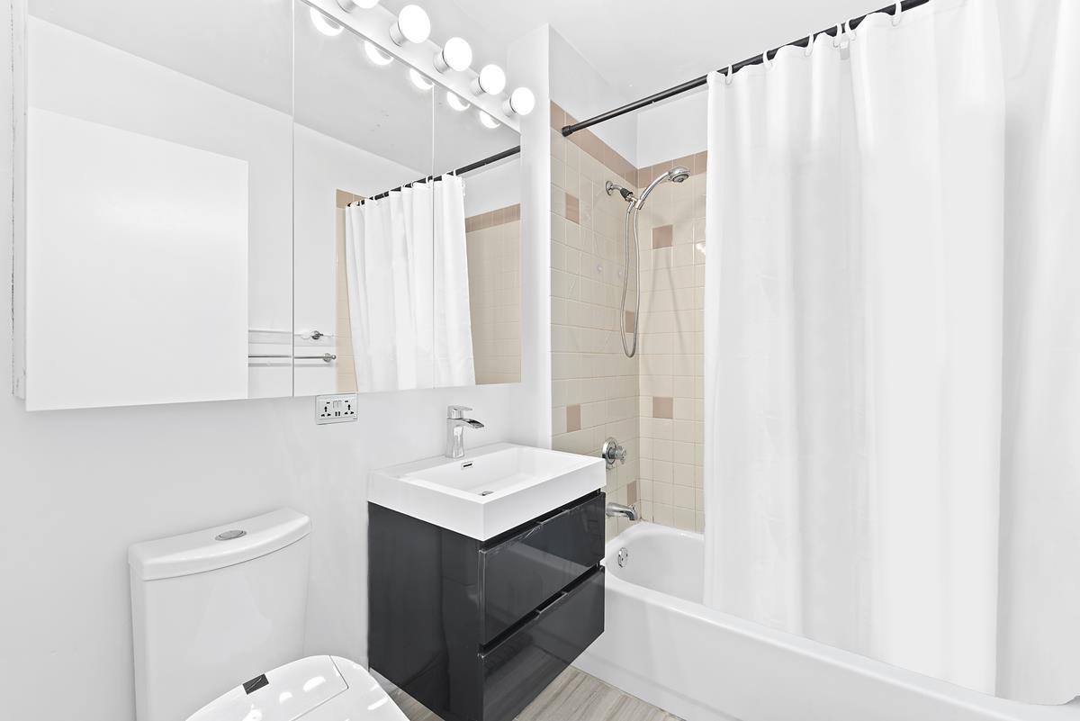 4-74 48th Avenue, Unit 26J Queens, NY 11109 - Photo 6 of 7 a bathroom with a sink a toilet and shower