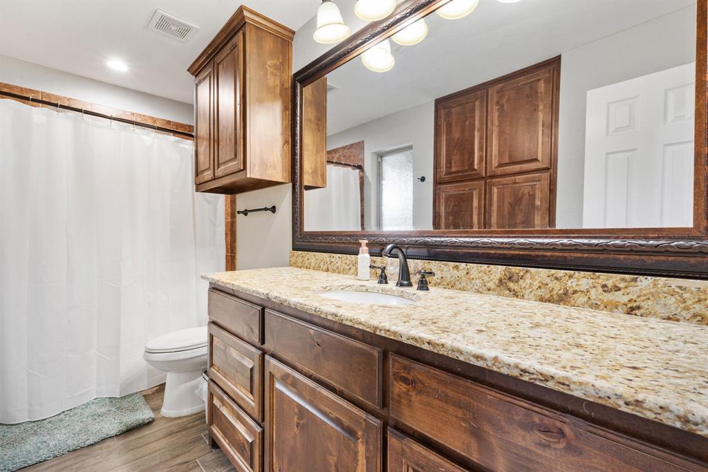 1407 Withers Road Mineral Wells, TX 76067 - Photo 23 of 38 a bathroom with a granite countertop sink a toilet and a mirror