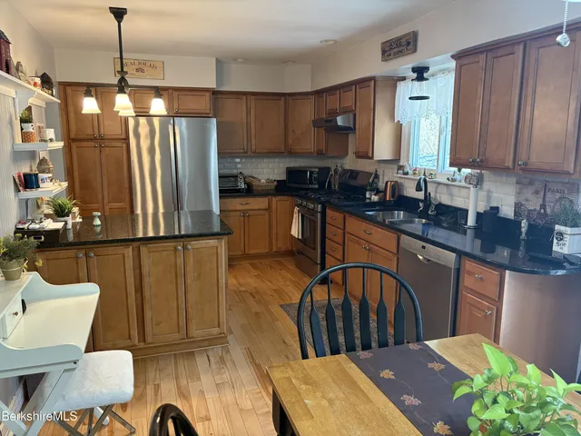 a kitchen with stainless steel appliances granite countertop a sink dishwasher a refrigerator with wooden cabinets and floor