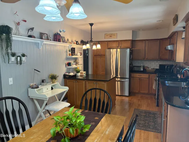 a kitchen with stainless steel appliances granite countertop a refrigerator a sink dishwasher a dining table and chairs with wooden floor