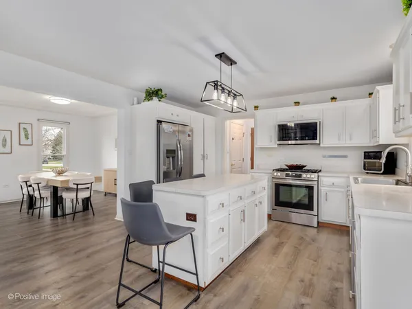 a large white kitchen with stainless steel appliances granite countertop a stove a sink dishwasher a dining table and chairs with wooden floor