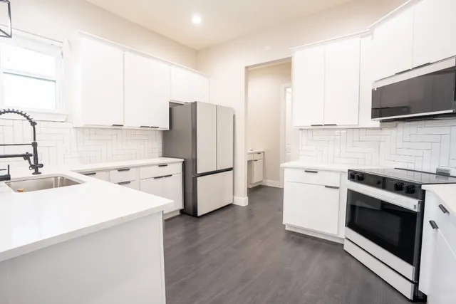 a kitchen with stainless steel appliances a stove a sink a refrigerator white cabinets and wooden floor