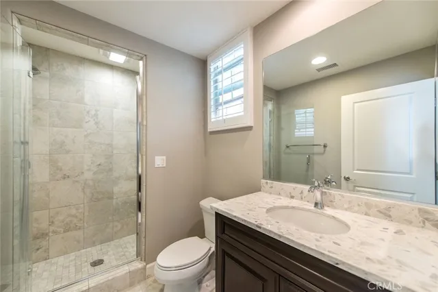 a bathroom with a granite countertop sink a toilet a mirror and shower