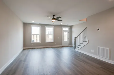 an empty room with wooden floor chandelier fan and windows