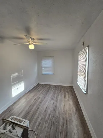 an empty room with wooden floor fan and windows