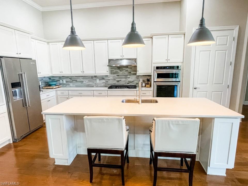 16163 Cartwright Lane Naples, FL 34110 - Photo 11 of 35 a kitchen with kitchen island a stove a refrigerator a sink dishwasher a dining table and chairs with wooden floor
