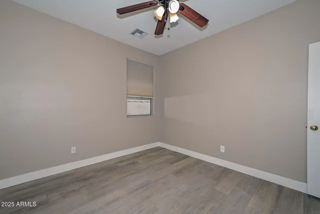 a view of an empty room with wooden floor and a chandelier fan