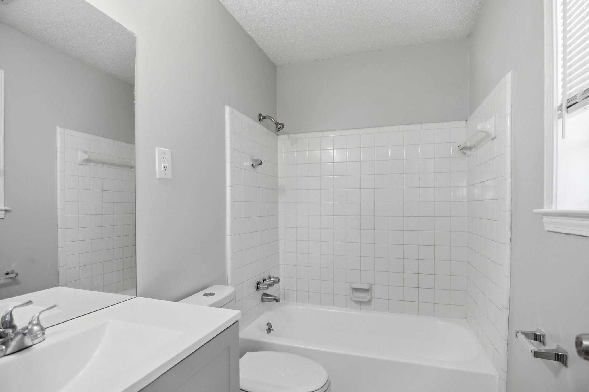 3113 Raleigh Ridge Cove Memphis, TN 38128 - Photo 34 of 38 Bathroom featuring a white bathtub with subway tile surround, chrome fixtures, a light gray vanity with an integrated sink, and a large wall mirror