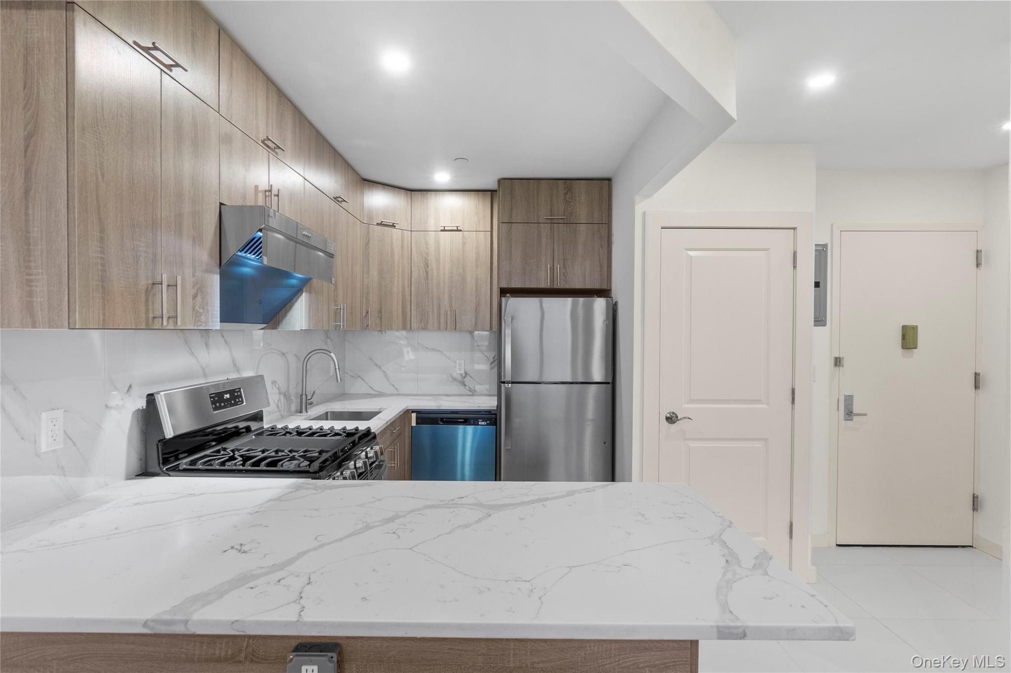 124-28 Queens Boulevard, Unit 10C Queens, NY 11415 - Photo 5 of 14 Kitchen with light stone counters, appliances with stainless steel finishes, tasteful backsplash, light tile patterned flooring, and a peninsula