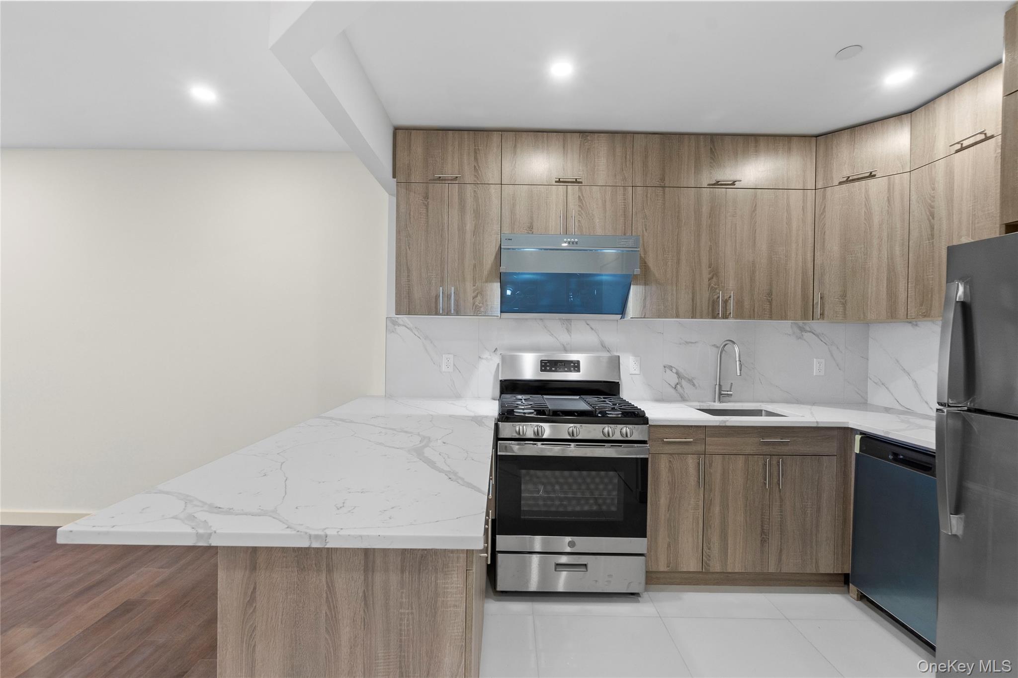 124-28 Queens Boulevard, Unit 10C Queens, NY 11415 - Photo 6 of 14 Kitchen with light stone counters, appliances with stainless steel finishes, tasteful backsplash, modern cabinets, and exhaust hood