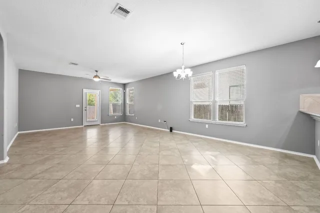 a view of an empty room with window and chandelier fan