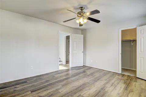an empty room with wooden floor chandelier fan and windows