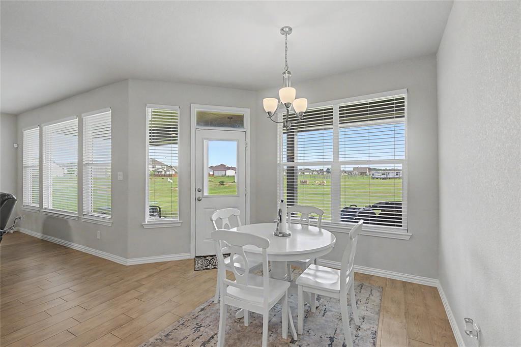 185 Chester Road Springtown, TX 76082 - Photo 22 of 40 Dining area featuring wood-finish flooring, light gray walls, multiple windows with blinds, a white exterior door with a transom window, and a chandelier