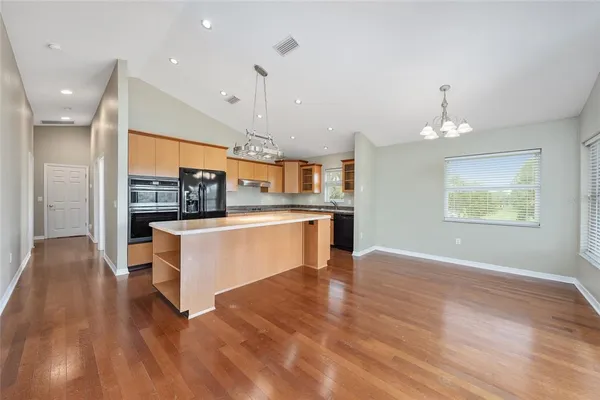 a kitchen with stainless steel appliances granite countertop a sink a stove a refrigerator and island with wooden floor