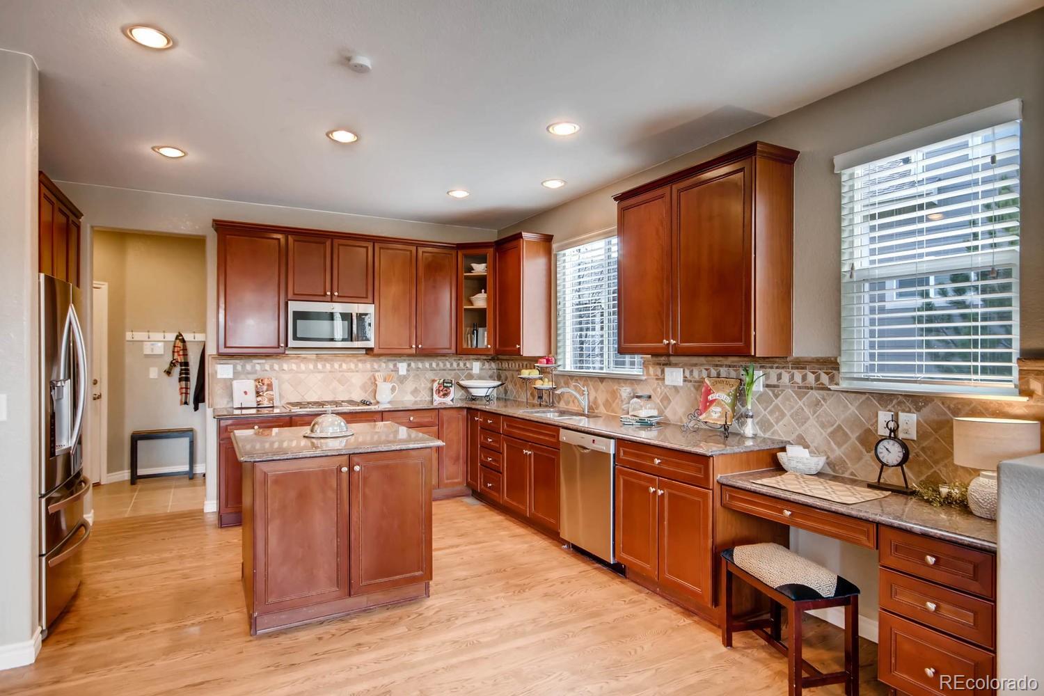 10951 Bluegate Way Highlands Ranch, CO 80130 - Photo 7 of 27 a kitchen with stainless steel appliances granite countertop wooden cabinets a sink a stove a refrigerator and island with wooden floors
