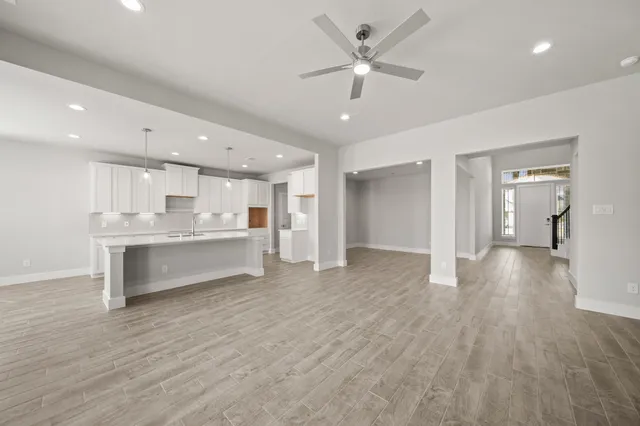a view of an empty room and kitchen view with wooden floor