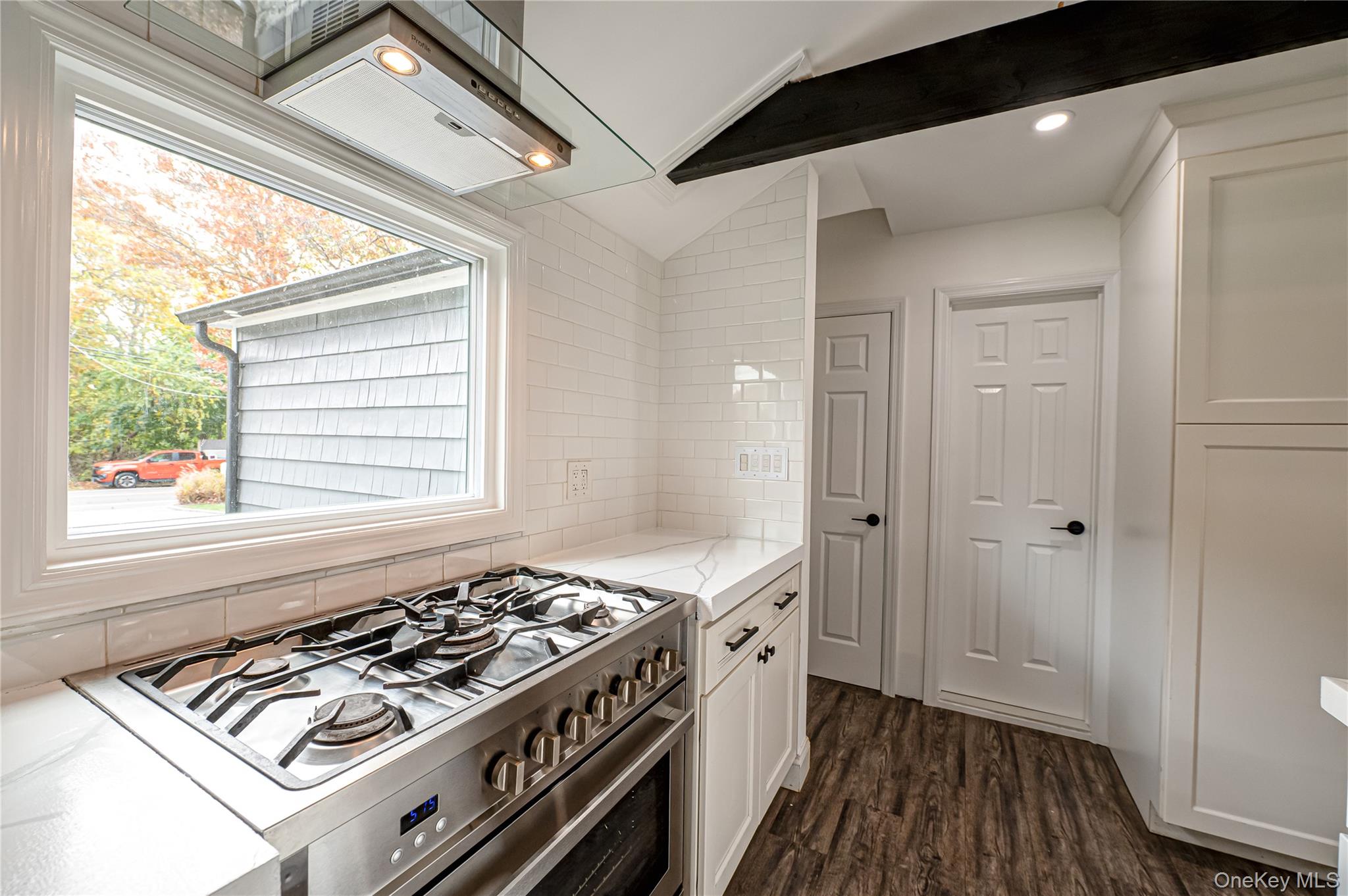 39 Lynncliff Road Hampton Bays, NY 11946 - Photo 9 of 34 Kitchen with stainless steel gas range, extractor fan, white cabinets, tasteful backsplash, and dark wood-style flooring