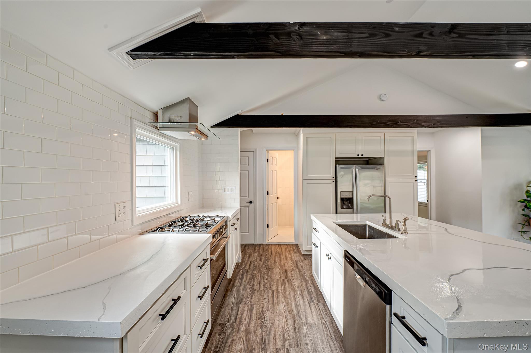 39 Lynncliff Road Hampton Bays, NY 11946 - Photo 10 of 34 Kitchen with decorative backsplash, white cabinets, dark wood-style flooring, light stone counters, and appliances with stainless steel finishes