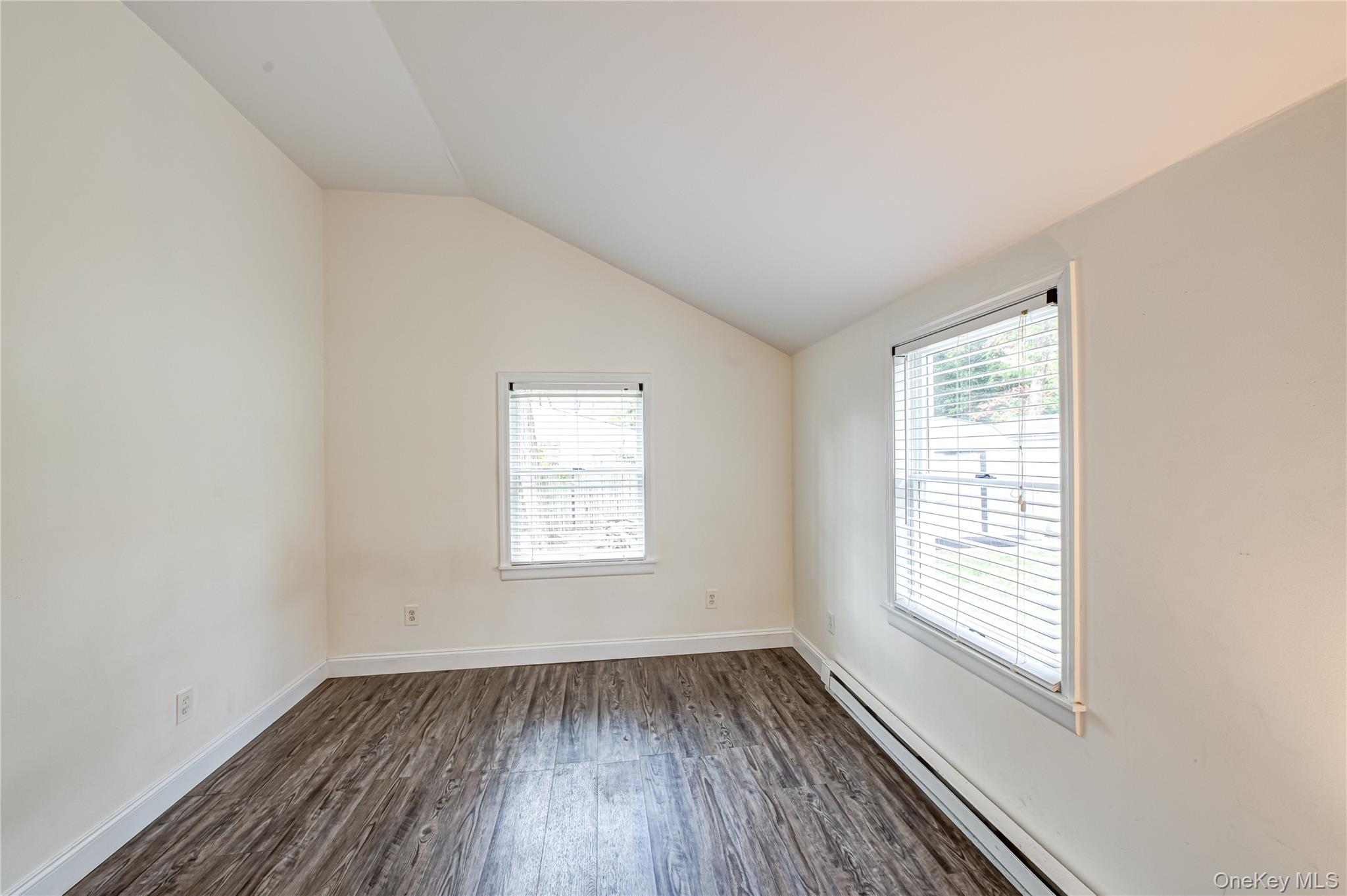 39 Lynncliff Road Hampton Bays, NY 11946 - Photo 16 of 34 Empty room featuring a baseboard heating unit, plenty of natural light, vaulted ceiling, and dark wood-style flooring