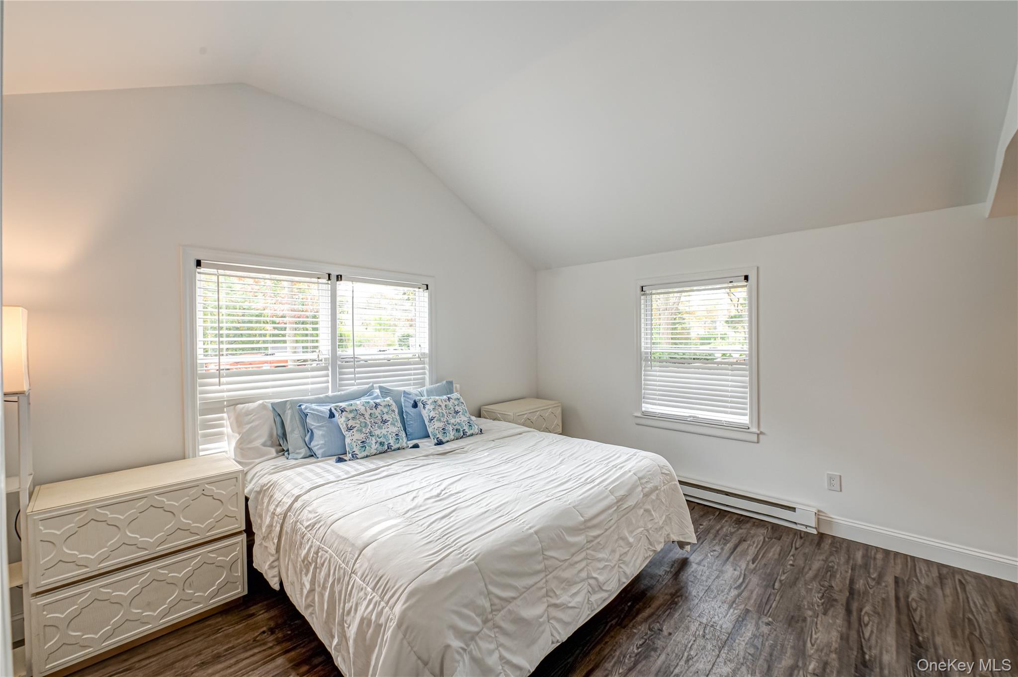 39 Lynncliff Road Hampton Bays, NY 11946 - Photo 17 of 34 Bedroom featuring dark wood-type flooring, a baseboard heating unit, lofted ceiling, and multiple windows
