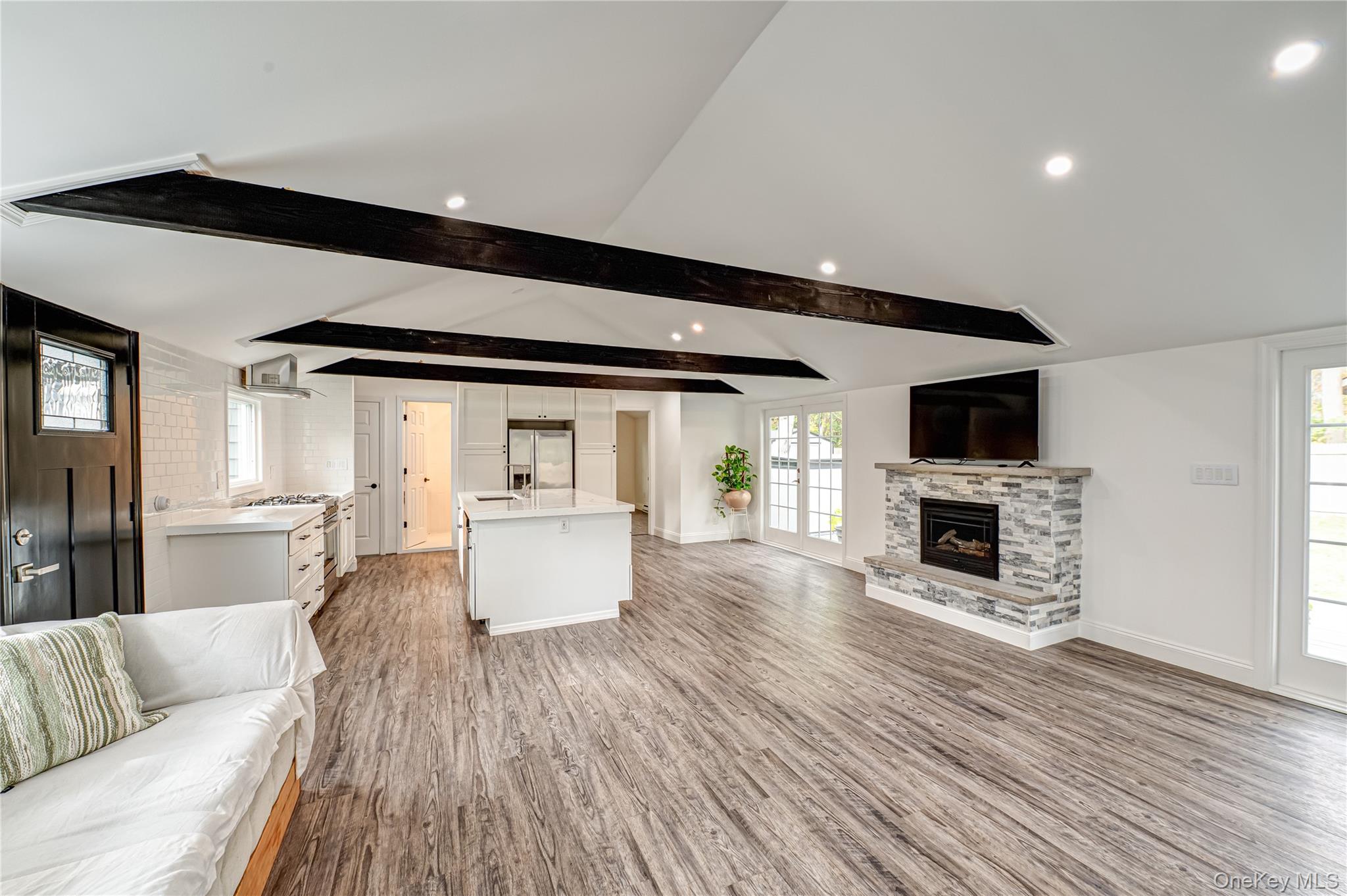 39 Lynncliff Road Hampton Bays, NY 11946 - Photo 6 of 34 Unfurnished living room with healthy amount of natural light, light wood-type flooring, beam ceiling, a stone fireplace, and recessed lighting