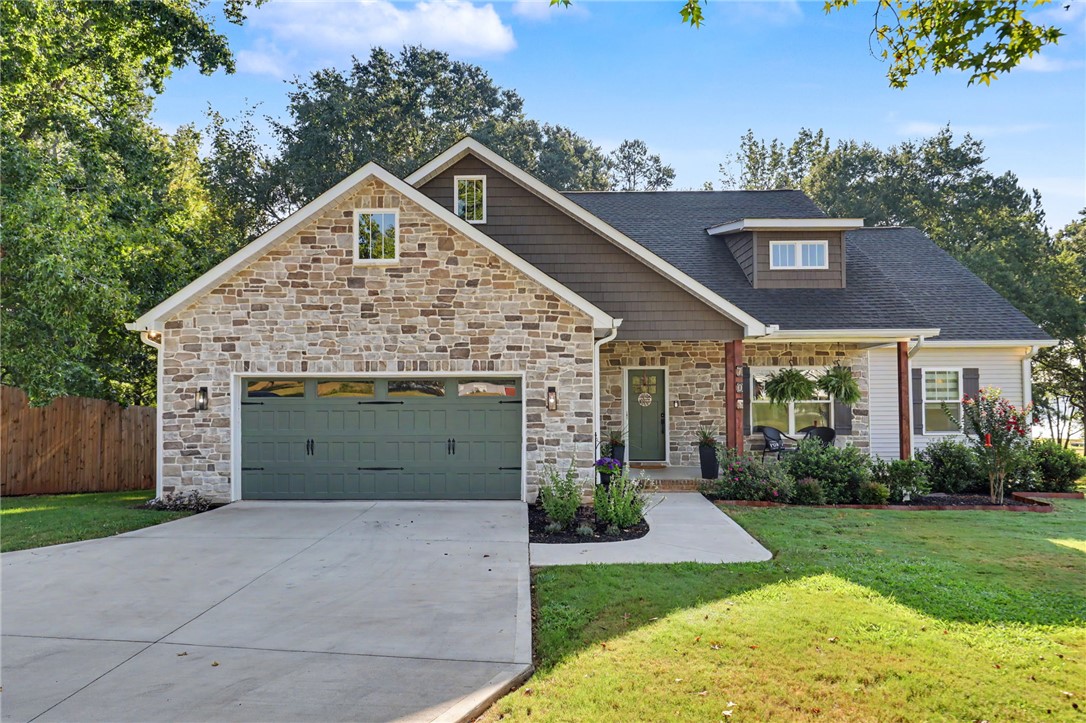 Natural stone and shake-style siding highlight the home’s inviting exterior, with a covered front porch and attached two-car garage.