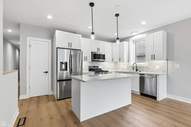 a kitchen with stainless steel appliances granite countertop a refrigerator a sink dishwasher a stove and white cabinets with wooden floor