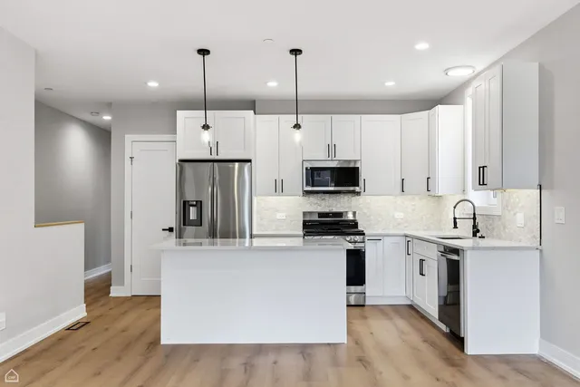 a kitchen with stainless steel appliances kitchen island granite countertop a sink a stove a refrigerator and white cabinets with wooden floor